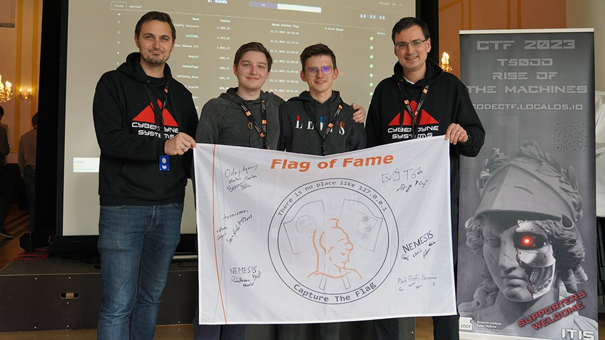 CODE-Geschäftsführer Marcus Knüpfer (l.) und der Leitende Direktor des FI CODE, Prof. Dr. Wolfgang Hommel (r.), überreichten zwei Vertretern des Siegerteams "Pink Fluffy Unicorns" (Mitte) die Flag of Fame. (Foto: © FI CODE)