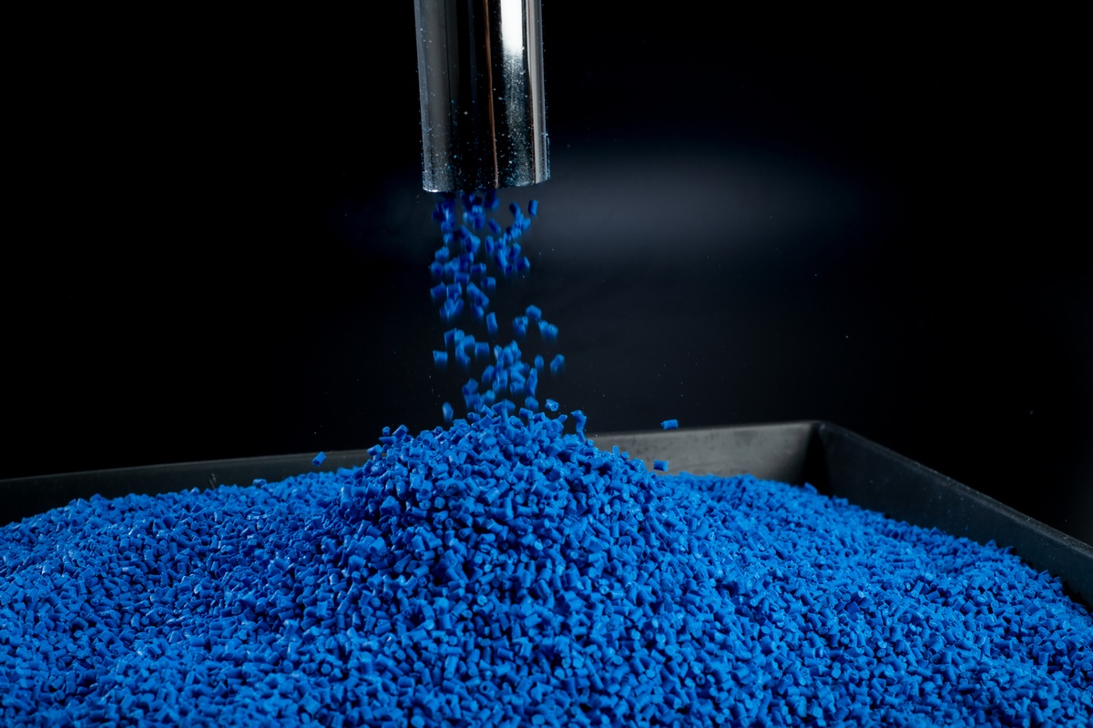 Polymergranulat, das durch ein Metallrohr auf ein schwarzes Tablett mit schwarzem Hintergrund fällt
