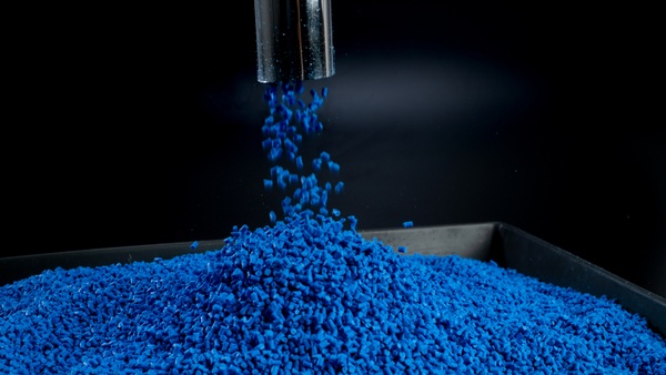 Polymergranulat, das durch ein Metallrohr auf ein schwarzes Tablett mit schwarzem Hintergrund fällt