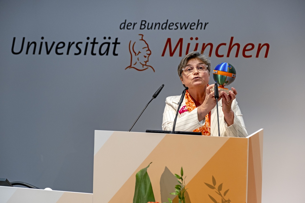 Prof. Deflers zeigt den Diversity-Ehrenpreis 2026 Prof. Deflers steht hinter einem Rednerpult. Sie hält den diesjährigen Diversity-Preis mit beiden Händen nach oben.