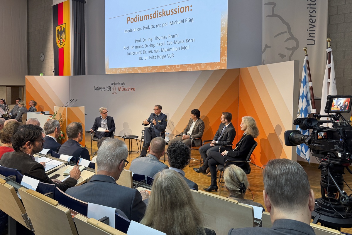 Podiumsdiskussion beim Dies academicus 2026 Im Vordergrund ist das Publikum im Audimax zu sehen. Vorne sitzen die vier Podiumsteilnehmer.