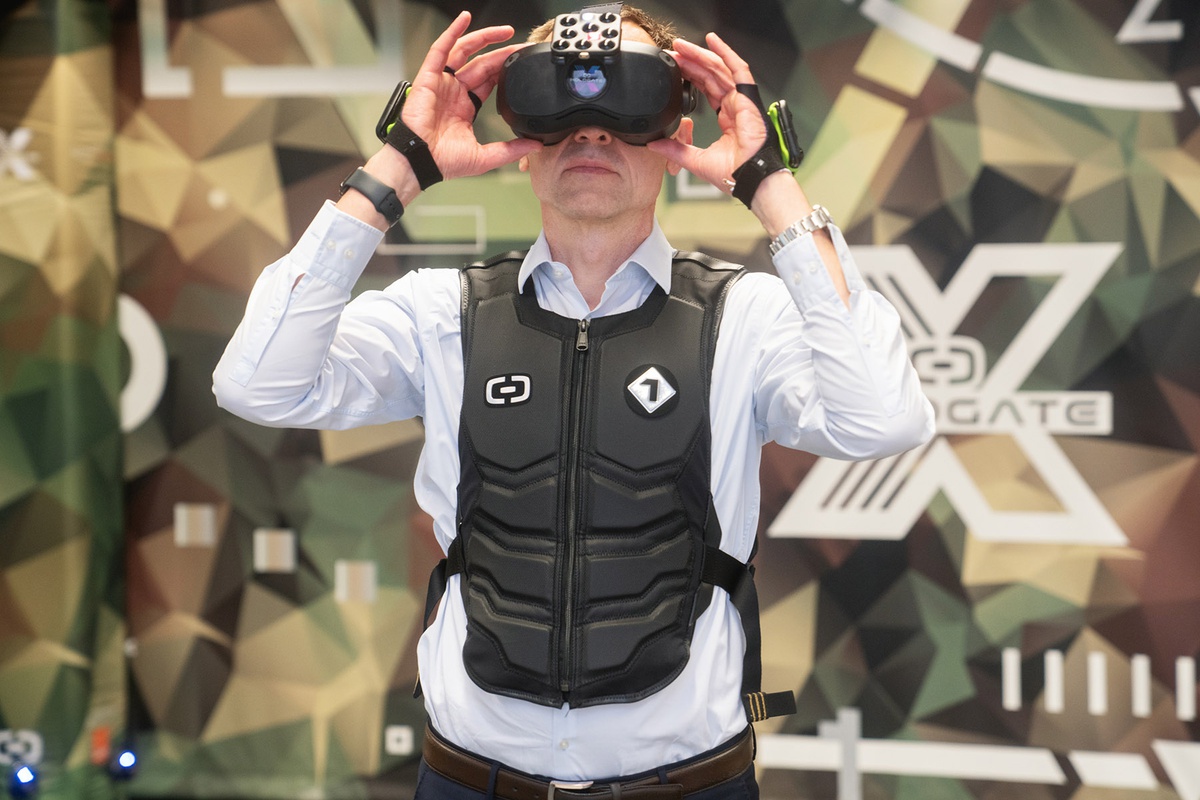 Prof. Kaisers trägt über seinem Hemd eine schwarze Sensoren-Weste und legt die Hände an die VR-Brille, die er trägt. An seinen Händen sind ebenfalls Sensoren angebracht.